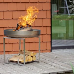 Vuurschaal NAGLIAI RVS met brandend houtvuur op een houten vlonder met houtopslag in het RVS onderstel